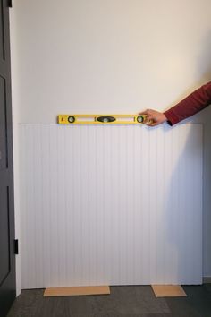 a person holding a tape measure in front of a wall with white boards on it