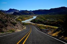 an empty road in the middle of nowhere with mountains in the background