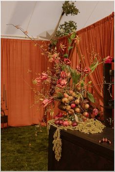 a vase filled with flowers sitting on top of a wooden table next to an orange curtain