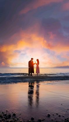 a man and woman standing on top of a beach next to the ocean at sunset