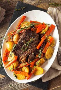 a white plate topped with steak, potatoes and carrots on top of a wooden table