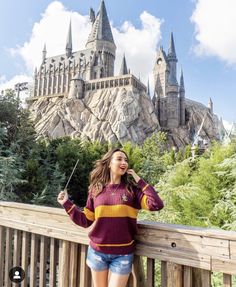 a woman standing next to a wooden fence in front of hog potter's castle