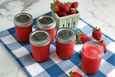 four jars filled with red liquid sitting on top of a blue and white checkered table cloth