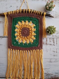 a crocheted sunflower is hanging on a wall next to succulents