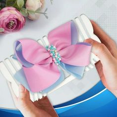 a person holding a pink and blue bow on top of a white plate with flowers in the background