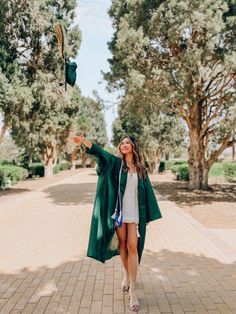 a woman in a graduation gown throwing a green cap into the air while standing on a brick walkway