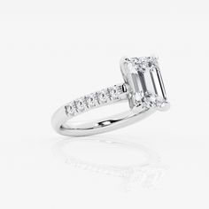 an emerald cut diamond engagement ring with side stones on the band and shoulders set in 18k white gold