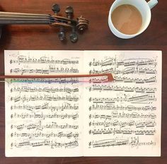 an old music sheet with musical notes next to a cup of coffee and a violin