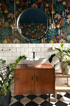 a bathroom sink sitting under a mirror next to potted plants and a wooden cabinet