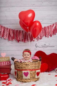 a baby sitting in a basket with red heart balloons