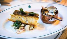 a white plate topped with fish and veggies next to a small bowl filled with sauce