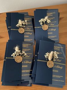 six navy blue and gold wedding cards with white flowers on the front, set on a wooden table