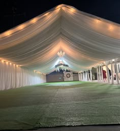 a large tent with white drapes and chandeliers on the ceiling is lit up at night