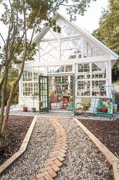 a white house with green doors and windows on the outside, surrounded by gravel path