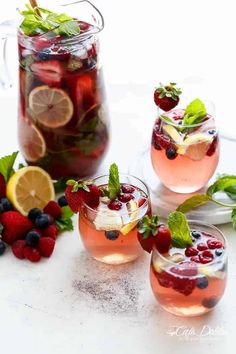 three glasses filled with fruit and ice on top of a white table next to sliced lemons