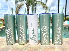 three personalized tumblers sitting next to a pool with palm trees in the background