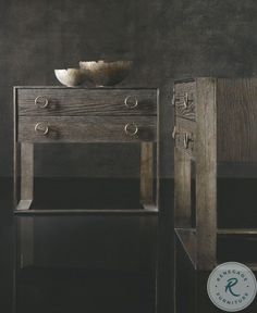 a wooden table with two drawers and a white bowl on it's top, against a dark background