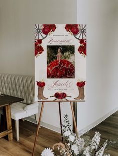 a white sign with a red dress and flowers in front of it on a wooden easel