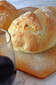 two loaves of bread sit on a cutting board next to a glass of wine