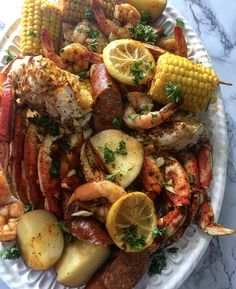 lobster, corn on the cob, and potatoes are served in a white platter