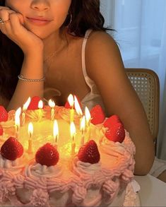 a woman sitting in front of a birthday cake with lit candles on it and looking at the camera