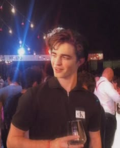 a young man holding a wine glass in his hand and smiling at someone behind him