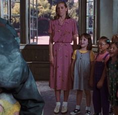 a group of children standing around each other in front of a woman wearing a pink dress