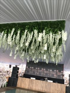 white flowers are hanging from the ceiling above a stage set up for a wedding reception