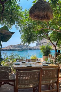 an outdoor dining area with table and chairs overlooking the water, surrounded by greenery