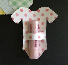 a pink lip balm bottle sitting on top of a piece of paper next to a baby's t - shirt