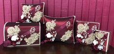 four decorative pillows on a table in front of a pink wall with red and white flowers