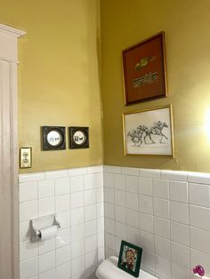 a white toilet sitting in a bathroom next to a wall with pictures hanging on it