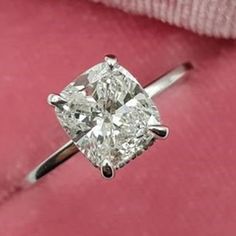 a cushion cut diamond sits on top of a pink velvet