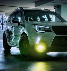 the front end of a white subarunt in a parking garage with its lights on