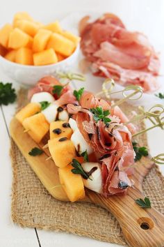 a wooden cutting board topped with fruit and meat