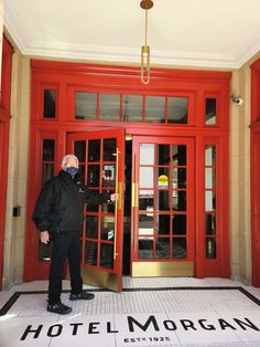 a man standing in front of a red hotel entrance with his hand on the door