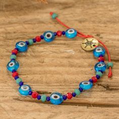 Keep those negative vibes away with a dapper creation by Ivania Ruiz from Guatemala. Working on red polyester threads, the artisan uses her professional eye to arrange a captivating combination of blue and green crystals around blue nazar glass beads, famous for working as amulets against the evil eye. The bracelet is also equipped with a sliding knot that allows you to adjust the length to your liking, making it perfect for an adventurous outing. In addition, a polished zamac charm dangles from the accessory as a sign of uniqueness. Negative Vibes, Glass Beaded Bracelet, Protection Crystals, Buy Crystals, Sliding Knot, Glass Beaded Bracelets, Amulets, Green Crystals, Blue Hues