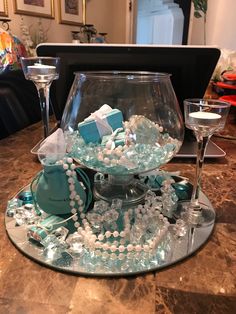 a glass bowl filled with pearls and other items on top of a table next to two wine glasses