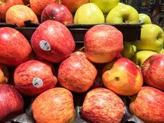 many red and green apples are stacked on top of each other in black bins