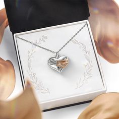 a heart shaped necklace in a box with ribbon around it and an angel wing on the front