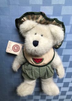 a white teddy bear wearing a green dress and hat with a tag on it's chest