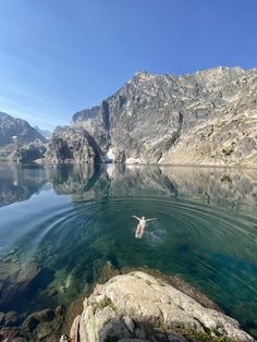 a person swimming in the water near some mountains