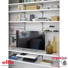 a flat screen tv sitting on top of a white shelf next to a bookcase