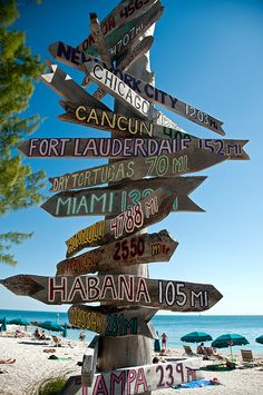 a wooden sign post with many different signs on it's side at the beach