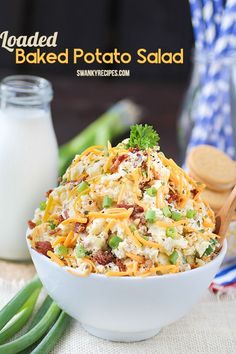 loaded baked potato salad in a white bowl with green onions and cheese on the side