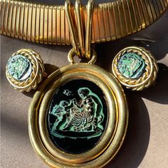 This Is An Impressive Vintage Set From Gerda Lynggaard Monies Series Of Jewelry Pieces. The Wide Stretch Gold Tone Necklace Is Graduated In Size From Front To Back And Has A Hook Closing. The Pendant Resembles An Aged Roman Coin With Faux Green Verdigris On The Black Figure Of Cupid And The Roman Goddess Aphrodite. Length 18” The Vintage Clip Earrings Are The Same Image Surrounded By Three Levels Of Detail Including Two Braided Metal Surroundings. All Three Pieces Are Reminiscent Also Of Cameos Bronze Spiritual Necklaces For Vintage Collection, Antique Necklaces With Coin-shaped Large Pendant, Ole Lynggaard Earrings, Collectible Vintage Bronze Necklace, Vintage Clip Earrings, Black Figure, Roman Goddess, Roman Coins, Two Braids