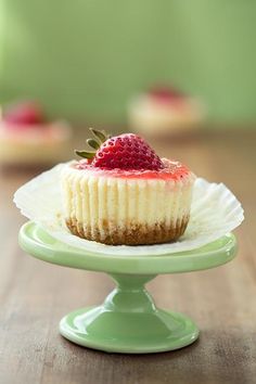 a small cupcake with a strawberry on top is sitting on a cake plate, ready to be eaten