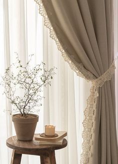 a small table with a vase and candle on it in front of a curtained window