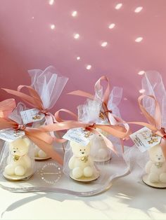 four small white teddy bears wrapped in organ bags with pink ribbons and tags on them