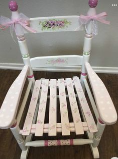 a white rocking chair with pink bows and polka dots on the bottom, sitting in front of a wall